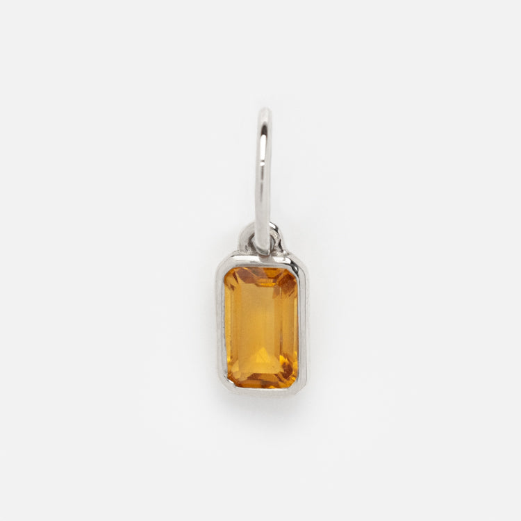 The Solid Gold Birthstone Baguette Charm in White Gold features a rectangular gemstone set in a minimalist white gold bezel with a small loop for easy attachment, perfect for personalized jewelry lovers and shown on a white background.