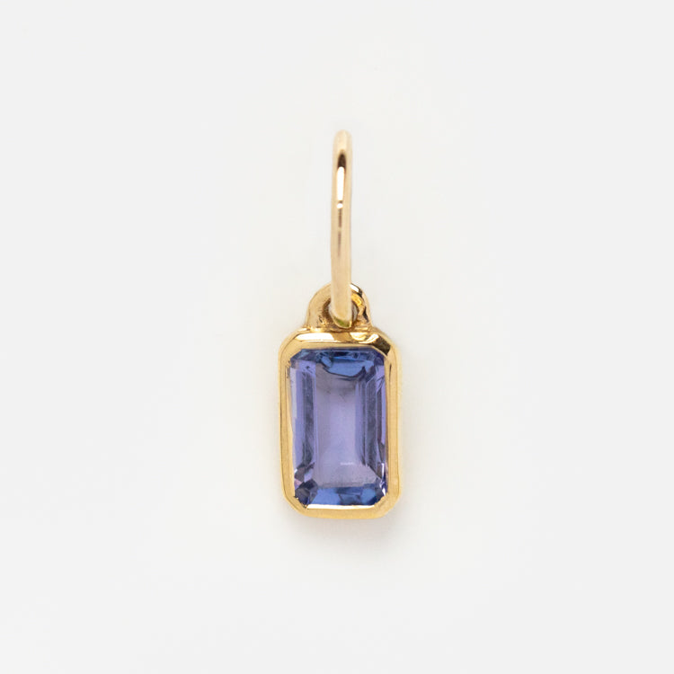 The Solid Gold Birthstone Baguette Charm features a faceted blue gemstone in a gold bezel setting with a simple loop, perfect for easily adding personalized elegance to your jewelry collection.