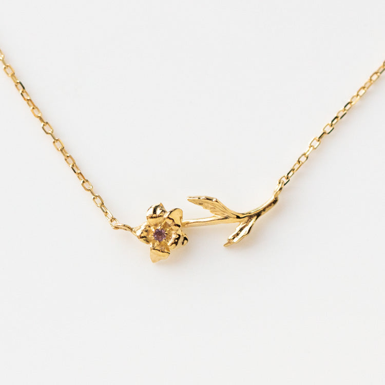 The Solid Gold Birth Flower February Necklace Sample is a delicate yellow gold pendant with a daffodil-shaped charm and a small amethyst center, set on a fine chain and shown against a white background.