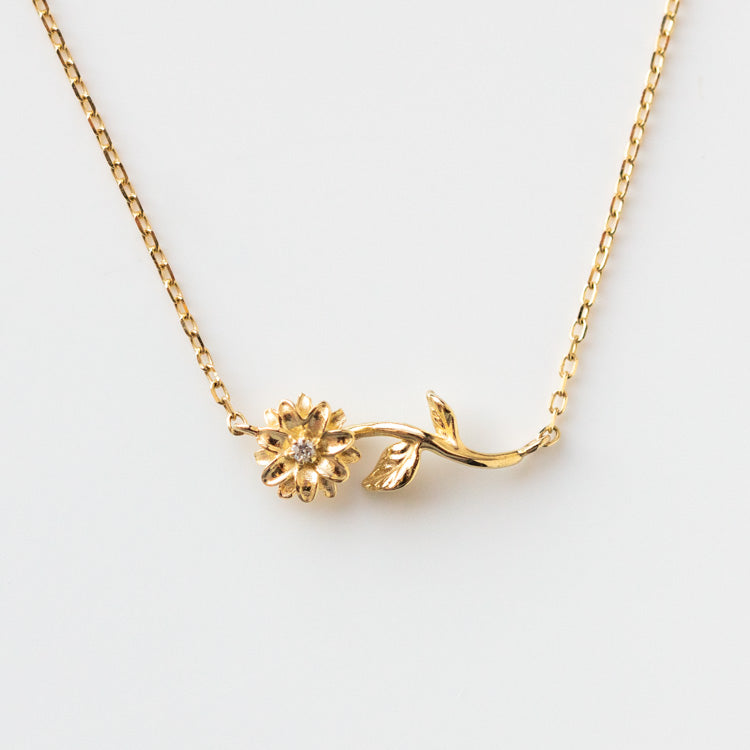 The Solid Gold Birth Flower April Necklace Sample is a delicate 9k yellow gold pendant with a small flower and leaf on a curved stem, shown against a plain white background.