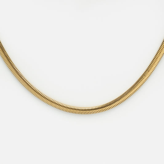 A close-up of the Classic Snake Chain Necklace, gold plated and perfect for layering with your favorite herringbone chain, arranged in a gentle curve on a plain white background.