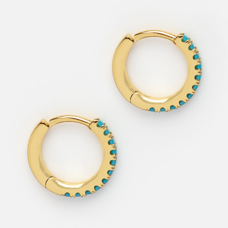 Classic Gem Huggie Hoops are 14k gold plated earrings featuring small turquoise stones along one edge, ideal for stacking and showcased on a white background.