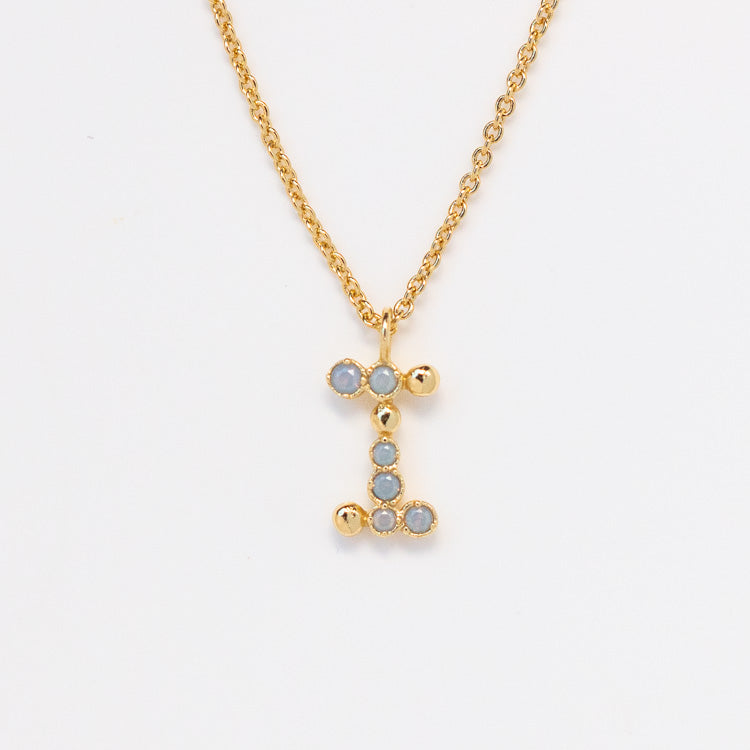 The Initial Charm Necklace Sample features a 14k yellow gold plated brass chain with an I-shaped pendant, detailed with light blue opalescent nano gems. Displayed on a plain white background.