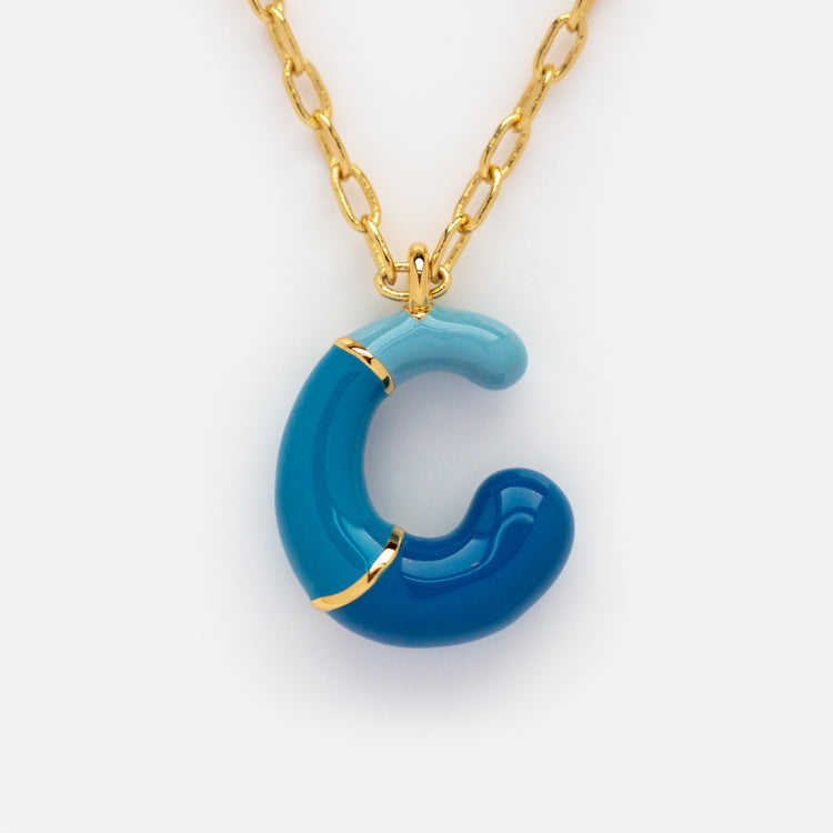 The Bubble Letter Necklace features a gold chain and a two-tone blue glass letter C pendant with gold metal accents, offering playful color and luxe style.