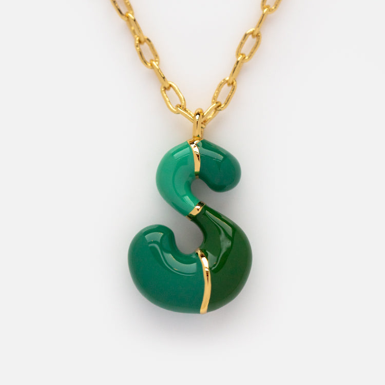 The Bubble Letter Necklace is a 14k gold plated piece with an S-shaped pendant, showing off two vibrant green hues divided by gold accents—a chic twist on the colorful letter necklace trend.