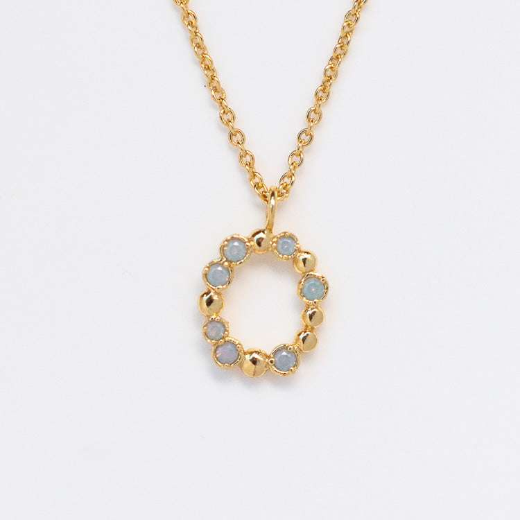 The Initial Charm Necklace Sample is a gold chain necklace with a circular pendant accented by opalescent nano gems in a 14k yellow gold plated brass ring.