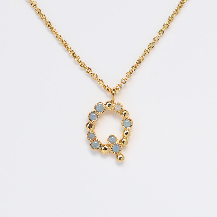 The Initial Charm Necklace Sample features a polished 14k yellow gold plated Q pendant with opalescent nano gems along the outline, hung on a shiny chain and brass base for an elegant finish.
