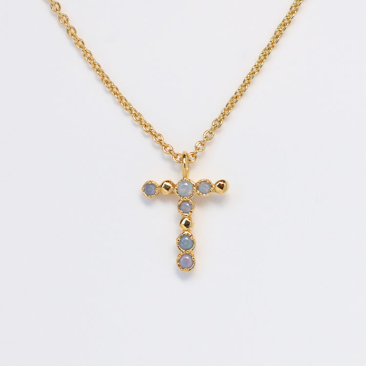 The Initial Charm Necklace Sample features a 14k yellow gold plated chain with a cross-shaped opalescent nano gems pendant on a brass base, accented with small round opal stones and shown against a plain white background.