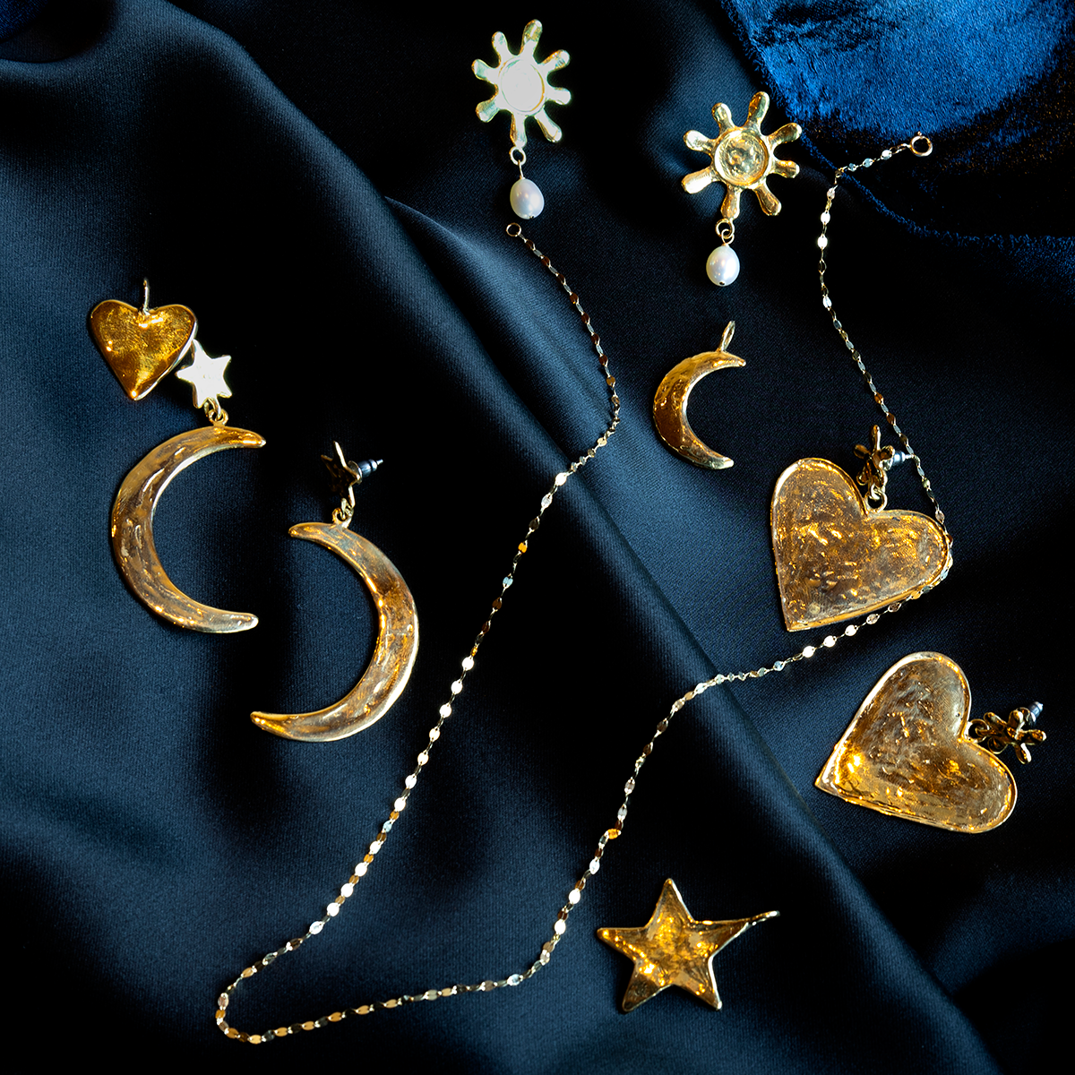The Luiny x Local Eclectic Bold Flower Heart Drop Earring, a handcrafted gold statement piece with a hammered texture, is displayed on dark blue satin fabric.