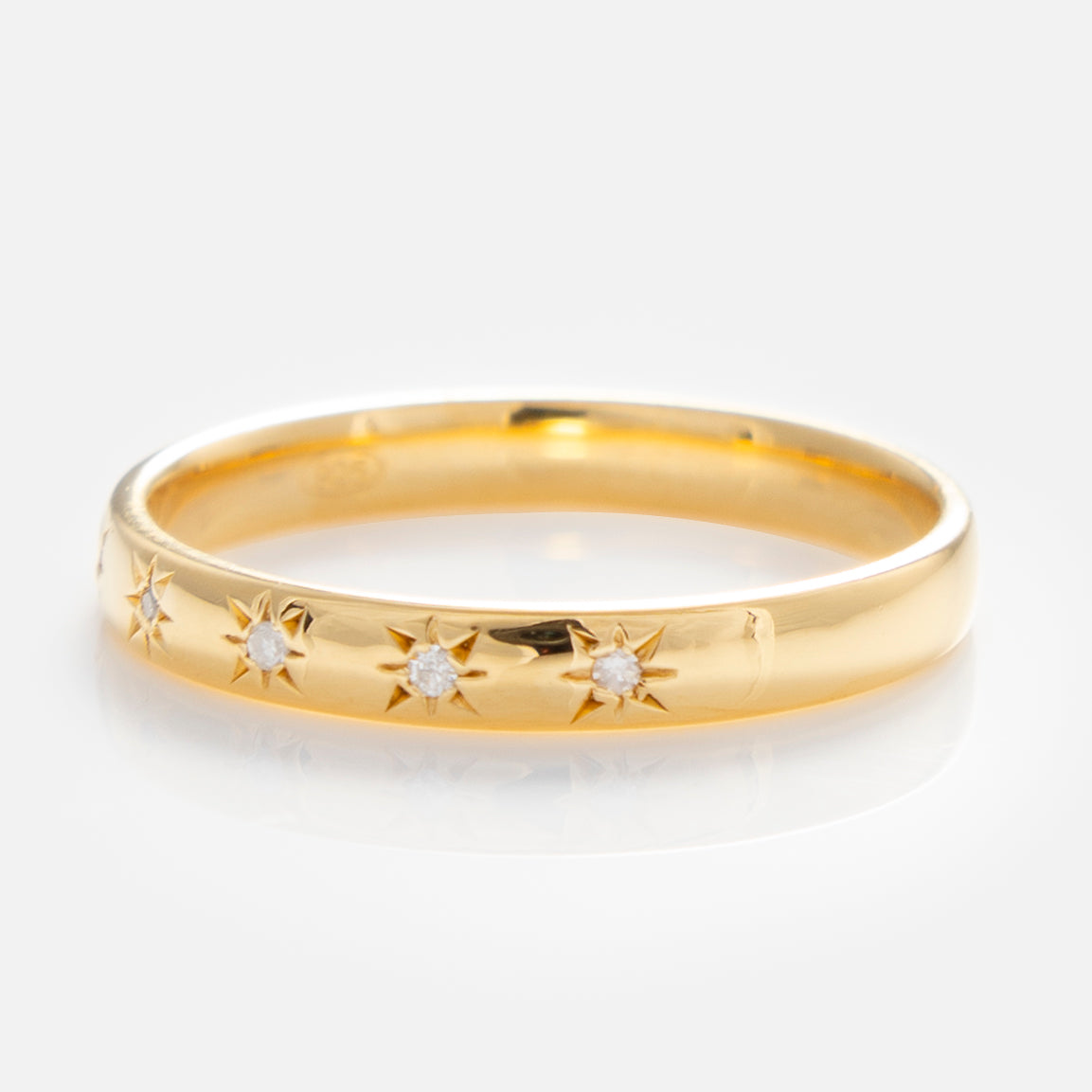 The Simple Star Set Diamond Band is a polished yellow gold vermeil pinky ring featuring five small diamonds in engraved starburst patterns, evenly spaced around the band and shown on a reflective white surface.