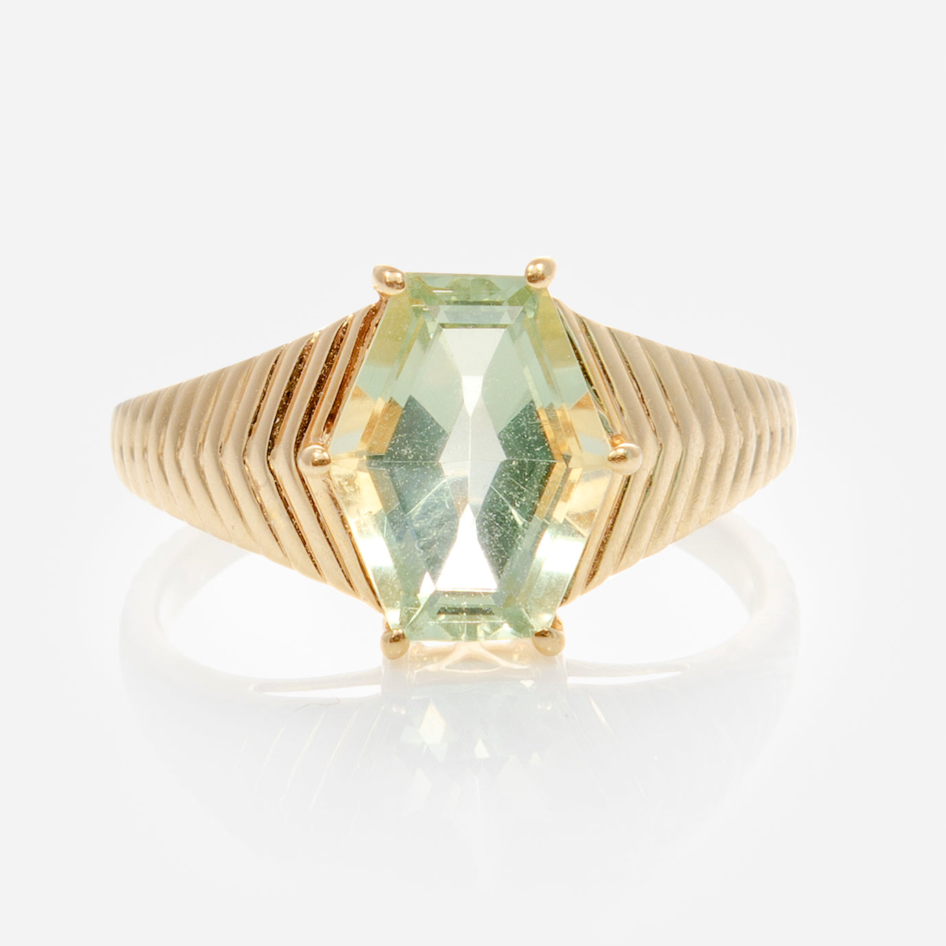 The Solid Gold Green Amethyst Bold Chevron Ring features a light green, hexagonal amethyst centerpiece set in 9k yellow gold with chevron accents and stepped, angular band detailing fanning out from the stone.