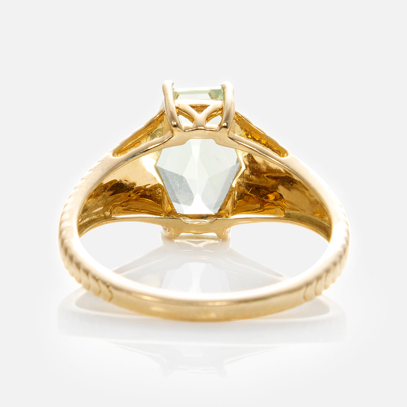 The Solid Gold Green Amethyst Bold Chevron Ring features a 9k yellow gold band with chevron accents and a light green, hexagon-cut gemstone in a raised prong setting, shown from beneath to display the intricate band and faceted gem underside.