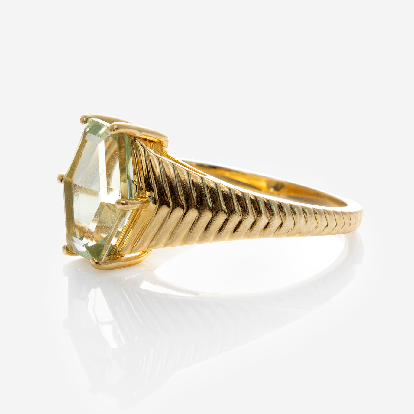 The Solid Gold Green Amethyst Bold Chevron Ring features a wide, textured 9k yellow gold band and a large, pale green hexagonal gemstone in a prong setting, shown on a white background.
