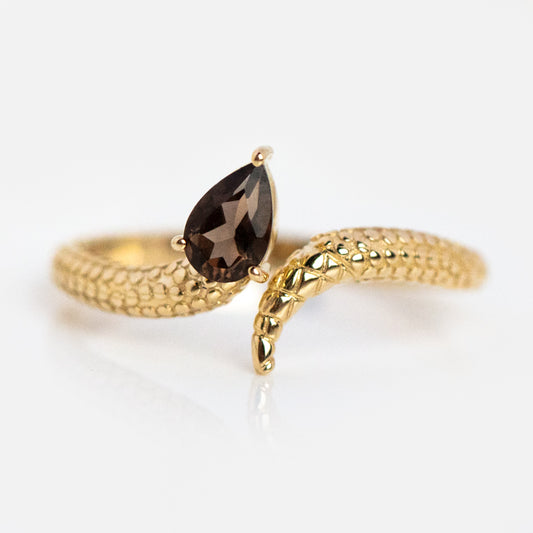 The Solid Gold Smoky Quartz Snake Ring for Transformation features a textured, snake-inspired band with a teardrop-shaped smoky quartz at the serpent’s head, displayed on a white background.