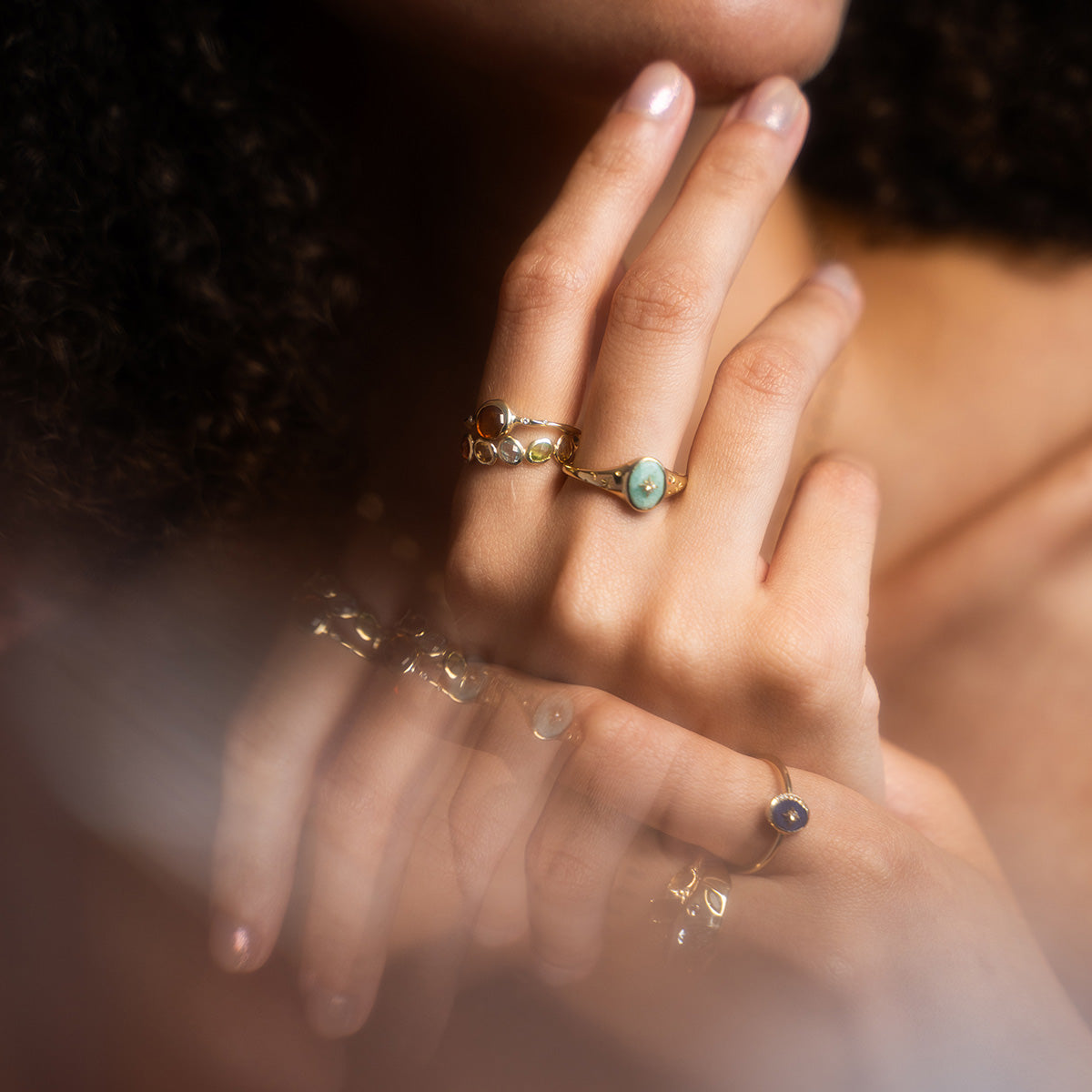 A close-up of a hand wearing the Solid Gold Crystal Signet Ring for Manifestation gently touches the face, with the rings elegant design reflected in a softly blurred surface below.