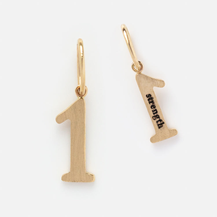 Two Solid Gold Number Charm pendants with small top loops are shown on a white background: one displays the front, while the other reveals the side engraved with strength—a unique numerology piece for personalized jewelry.