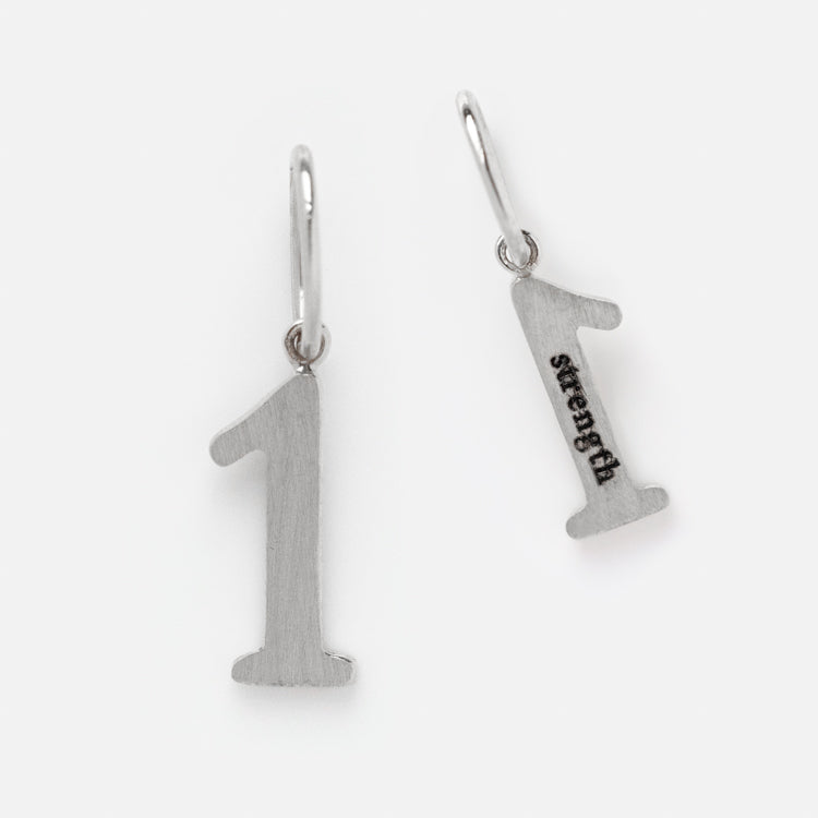 Two Solid Gold Number Charms in White Gold, each with a top loop—one plain and one engraved with Strength—are shown on a white background. A distinctive addition to personalized jewelry collections.
