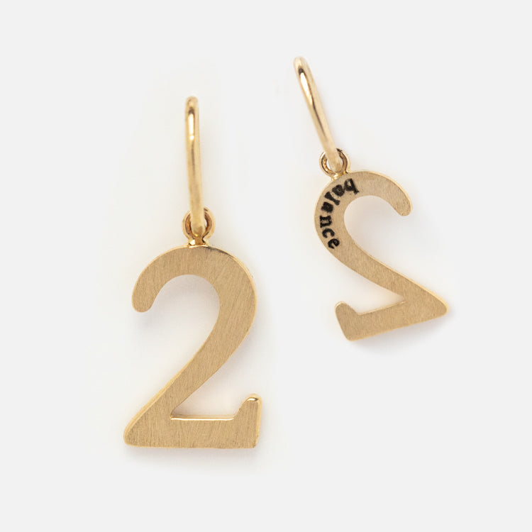 The Solid Gold Number Charm earrings feature a sleek number 2 design with an engraved mark inside one earring and simple gold hooks, offering a subtle, unique piece of personalized jewelry for numerology enthusiasts.