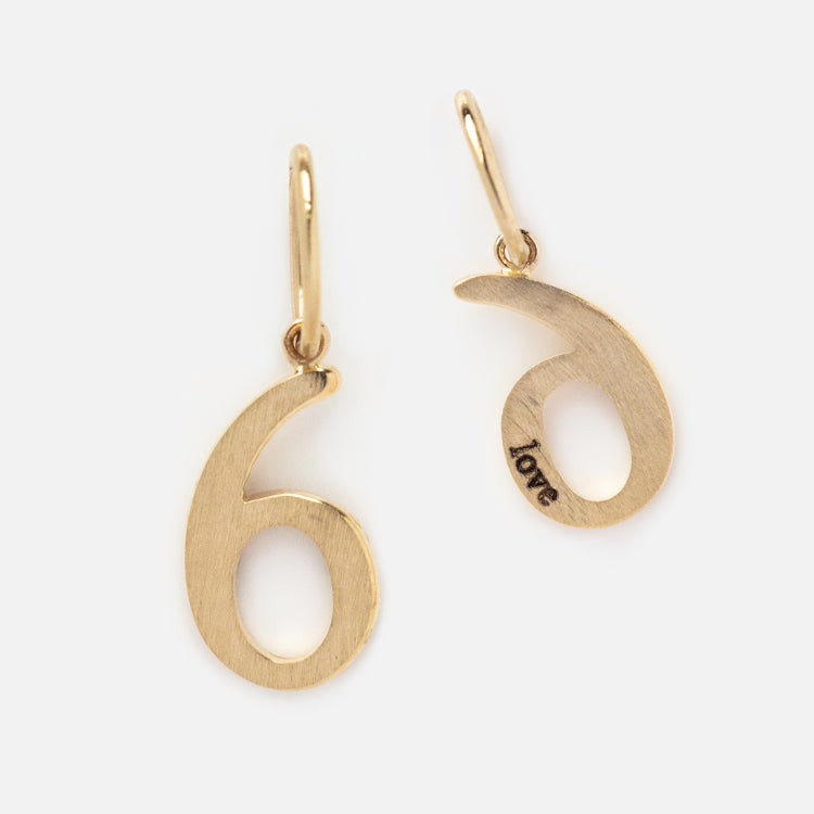 A pair of Solid Gold Number Charm earrings, shaped like the number six with an engraved love numerology charm on the inner curve, displayed against a simple white background.