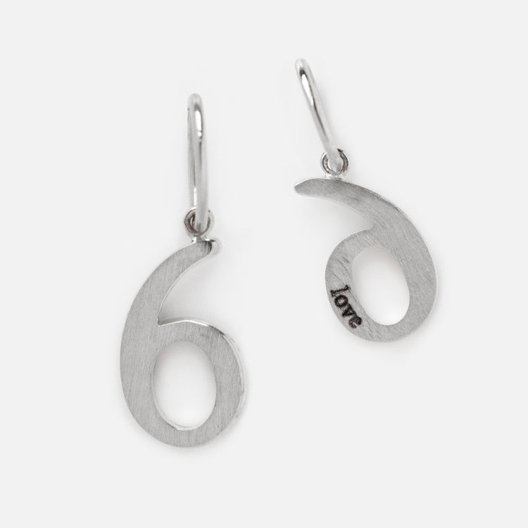 A pair of solid white gold number charm earrings shaped like the number six, one engraved with love on the inner curve. The brushed finish and simple hooks create elegant, personalized jewelry for any occasion.