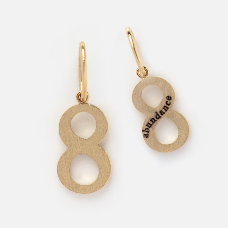 The Solid Gold Number Charm earrings are shaped like the number 8, with a numerology abundance charm and small hoops for easy wear.