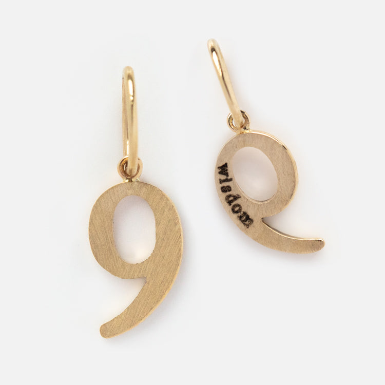 The Solid Gold Number Charm features two gold charms with small loops for attaching to jewelry. One has a plain front, and the other is engraved with wisdom on the back—perfect for creating meaningful, personalized accessories.
