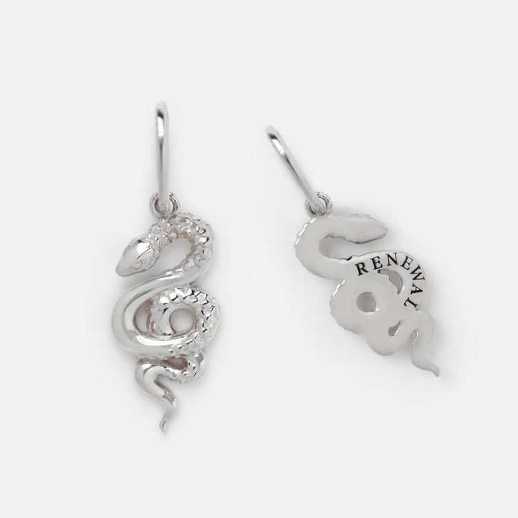 Two snake-shaped pendants in white gold, one showing the front and the other the back engraved with RENEWAL. Both have loops for attaching to jewelry and pair beautifully with pearl details or the Solid Gold Nature Charm in White Gold.