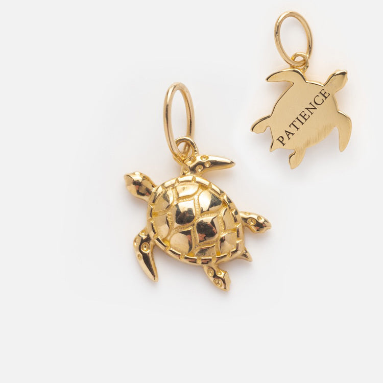 The Solid Gold Nature Charm is a turtle-shaped pendant featuring a detailed shell on one side and PATIENCE engraved on the other, with loops for attaching to a chain or bracelet.