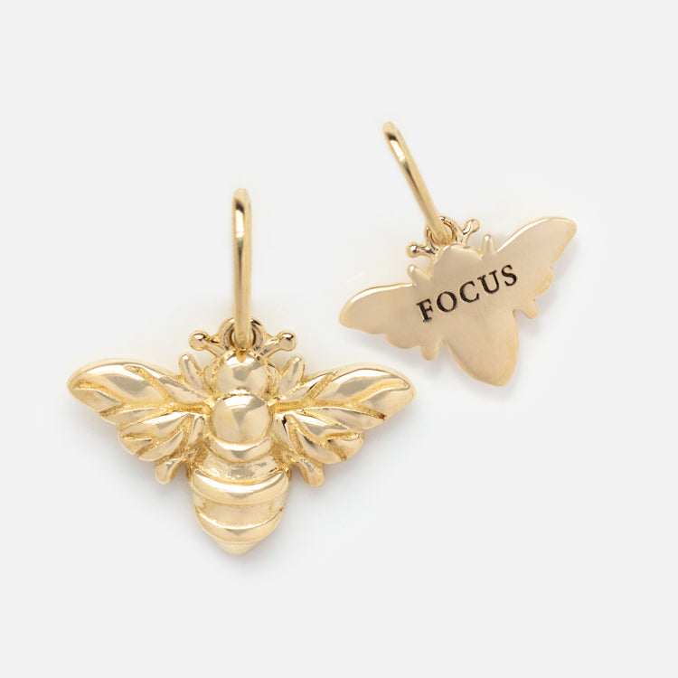 Two solid gold nature charms—one shaped like a bee with detailed front, the other engraved with FOCUS—make unique animal gold accents. Both include loops for attaching to spiritual jewelry or your favorite accessory.