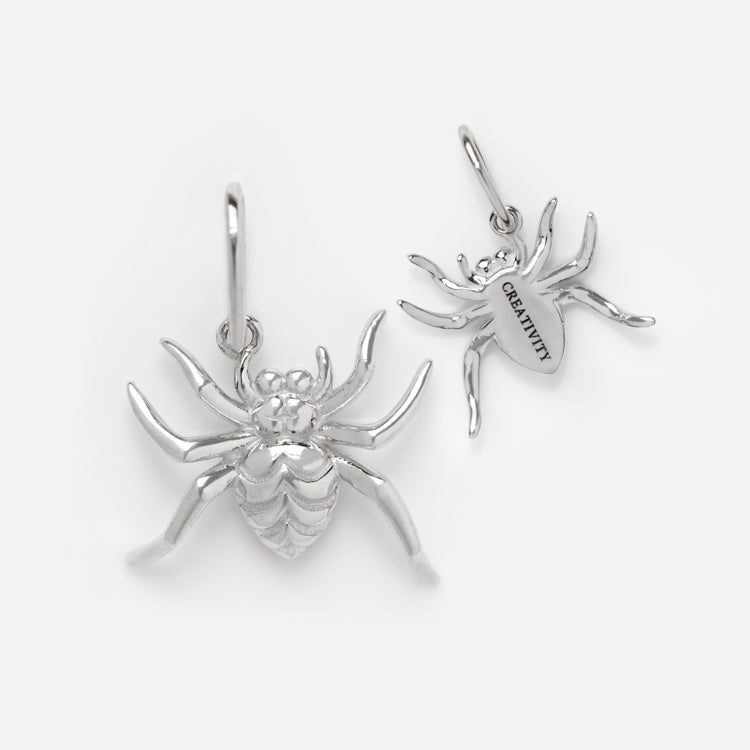 Two silver spider-shaped charms are displayed. One shows detailed legs and body, while the other reveals CREATIVITY engraved on its underside—a perfect Solid Gold Nature Charm in White Gold.