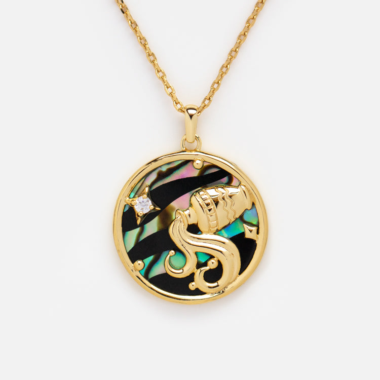 The Zodiac Pendant Necklace features a 14k gold-plated chain with a round abalone shell pendant, showcasing an elegant gold Aquarius symbol and a sparkling clear gemstone star.