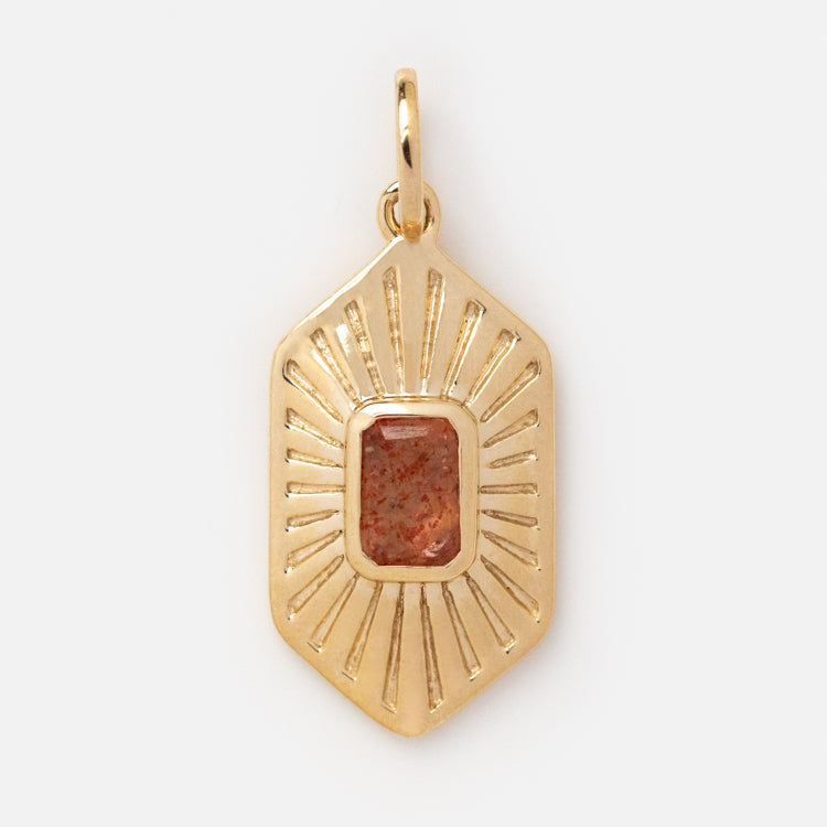 Exclusive to Local Eclectic, the Solid Gold Amulet Charm is an elongated hexagonal pendant with a rectangular reddish-brown gemstone at its center and engraved radiating lines.