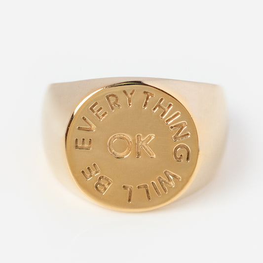 The Everything Will Be Ok Pinky Signet Ring features a round 14K gold-plated face engraved with “EVERYTHING WILL BE OK” in a circle around “OK” at the center, displayed on a plain white background.