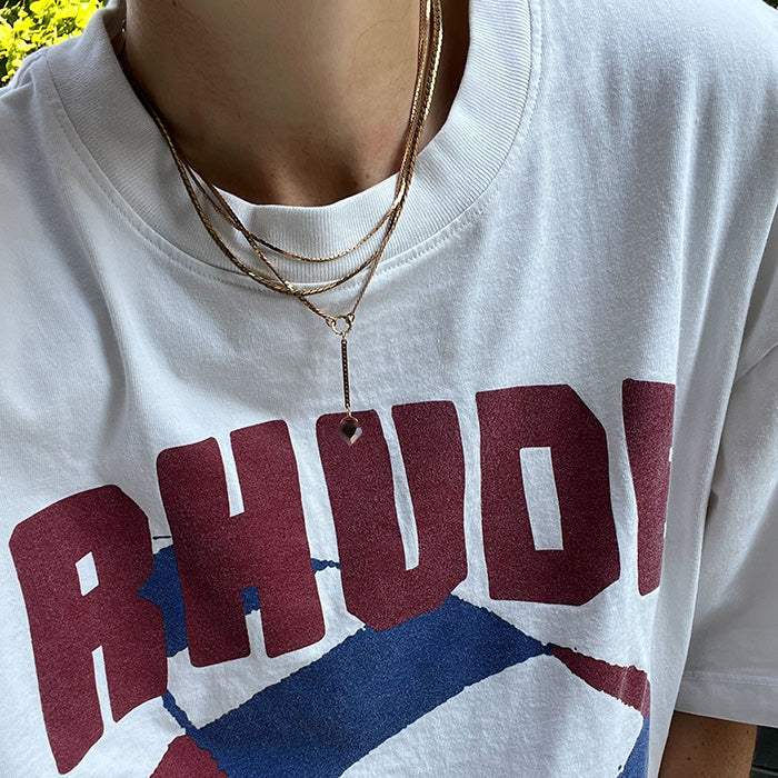 Close-up of a person in a white T-shirt with RHUDY in bold red letters and a blue graphic, styled with the Palmer Gemstone Necklace for a chic finishing touch.
