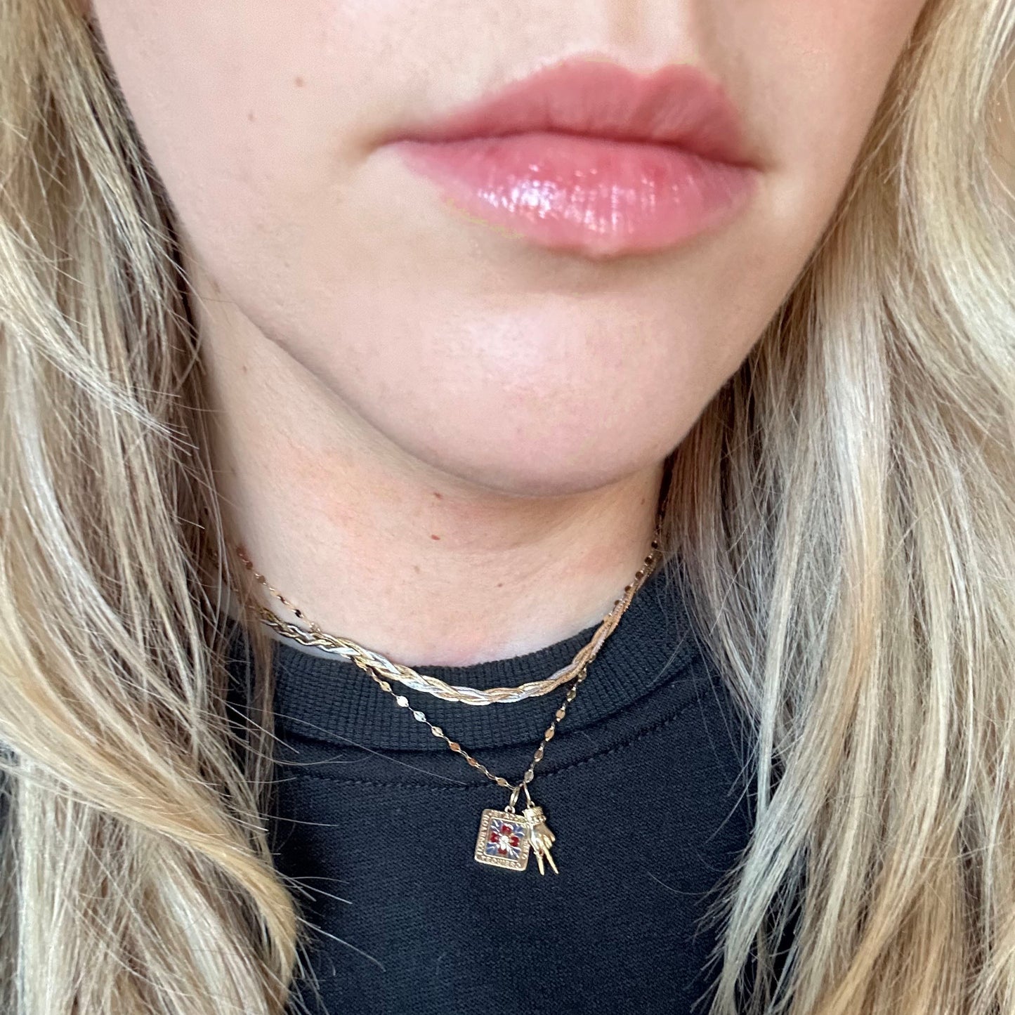 Close-up of a womans lower face with light pink glossy lips, long blonde hair, and wearing two gold necklaces—including the Solid Gold Body Language Charm—layered over a dark top.