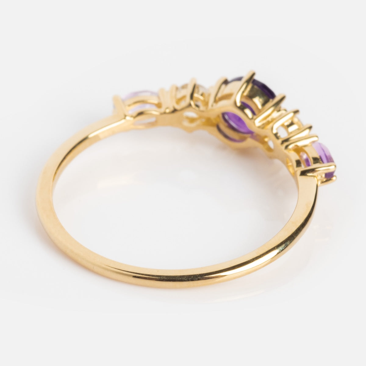 The Solid Gold 2025 February Capsule Classic Amethyst Statement Ring features a slim band adorned with multiple round purple gemstones in a row, making it an elegant February birthstone piece displayed on a white background.