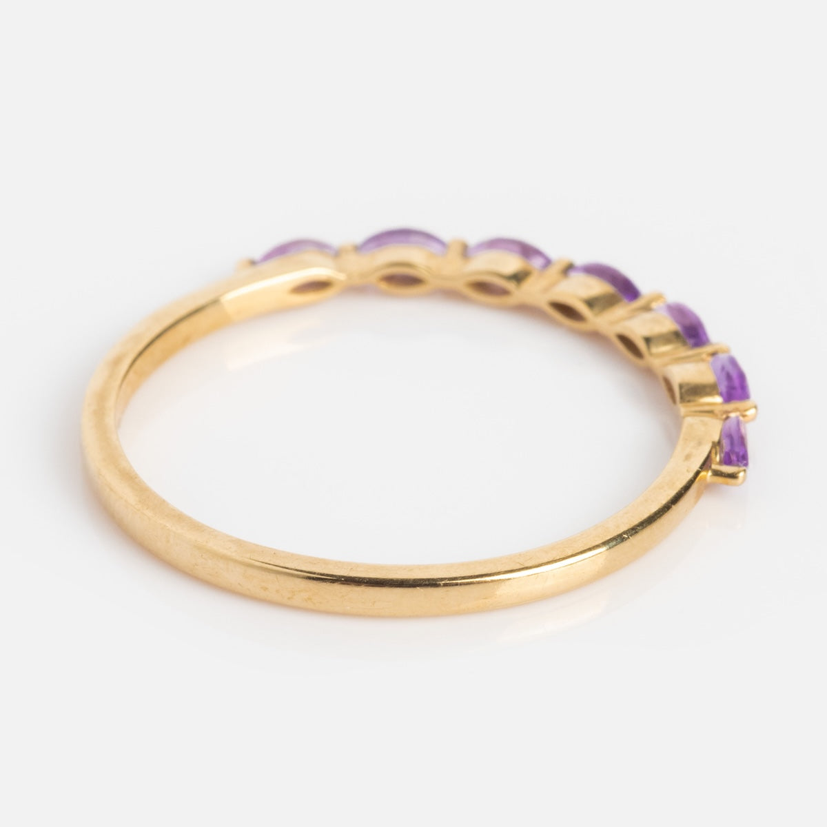 The Solid Gold 2025 February Capsule Delicate Amethyst Stacking Ring features a thin band with small oval purple amethysts, perfect for stacking, displayed on a white background.