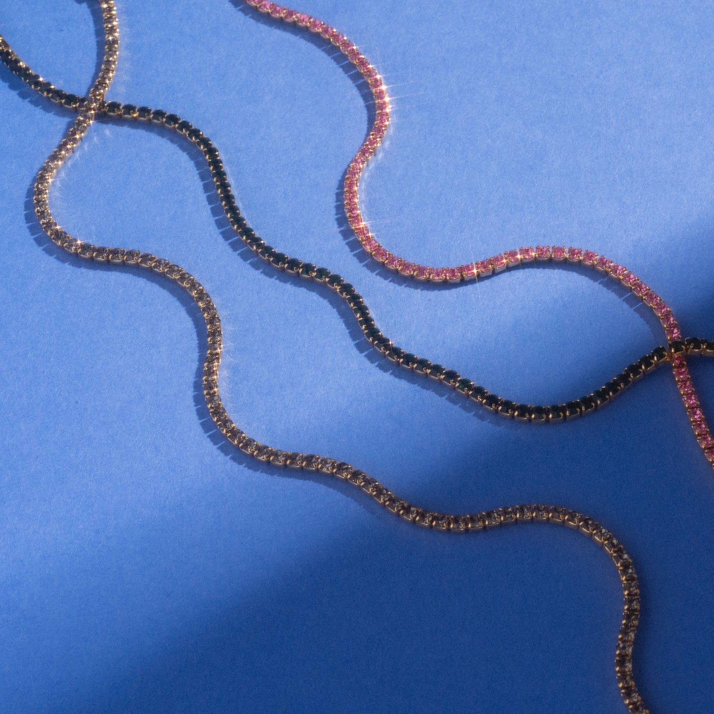 An Emerald CZ Tennis Bracelet Sample is displayed on a flat, blue background, its sparkling stones casting soft shadows.