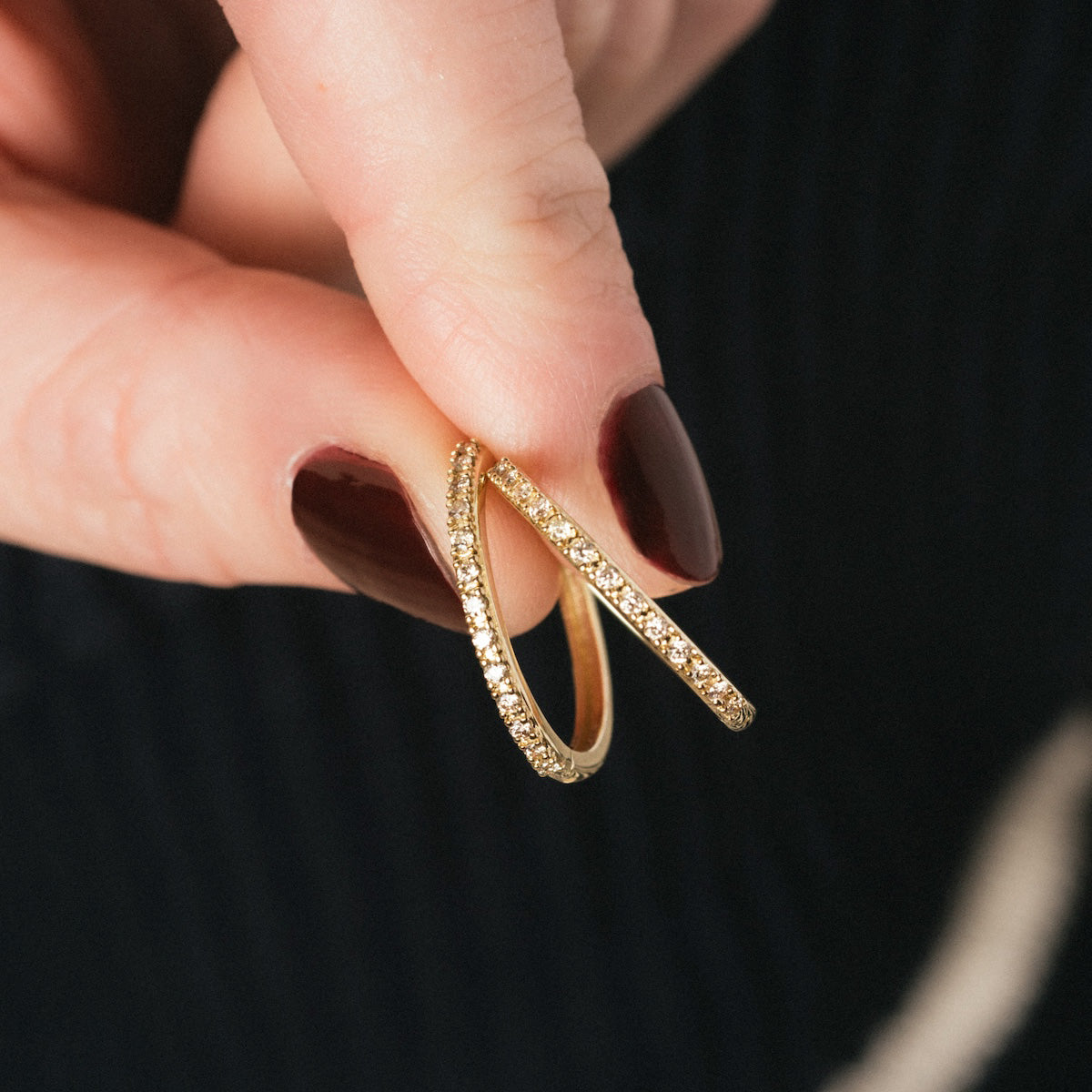 A hand with dark red nail polish holds a pair of Solid Gold Diamond Hoops, crafted in 10k solid gold and encrusted with sparkling lab-created diamonds.