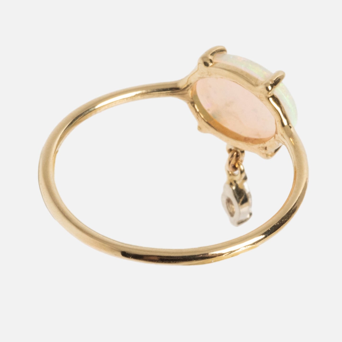 The One of a Kind 14k Opal with Diamond Dangle Ring features a delicate gold band with an oval opal in a prong setting and a small diamond charm that dangles beneath the stone.
