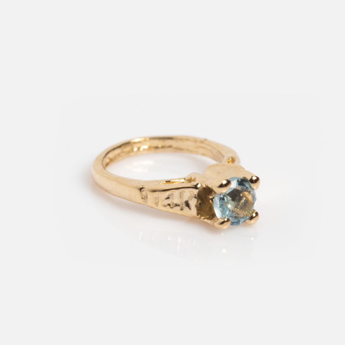 The 14k Littlest Birthstone Ring Charm by Charlie and Marcelle showcases a round light blue gemstone in a four-prong gold setting, shown against a white background.