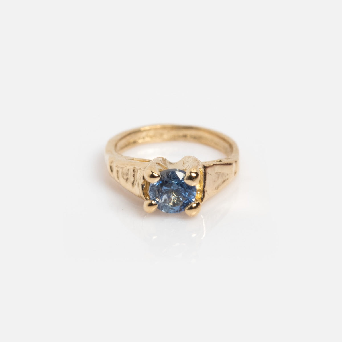 The 14k Littlest Birthstone Ring Charm by Charlie and Marcelle features a gold engraved band with a round blue gemstone in a four-prong setting, shown on a plain white background—a timeless, elegant birthstone piece.