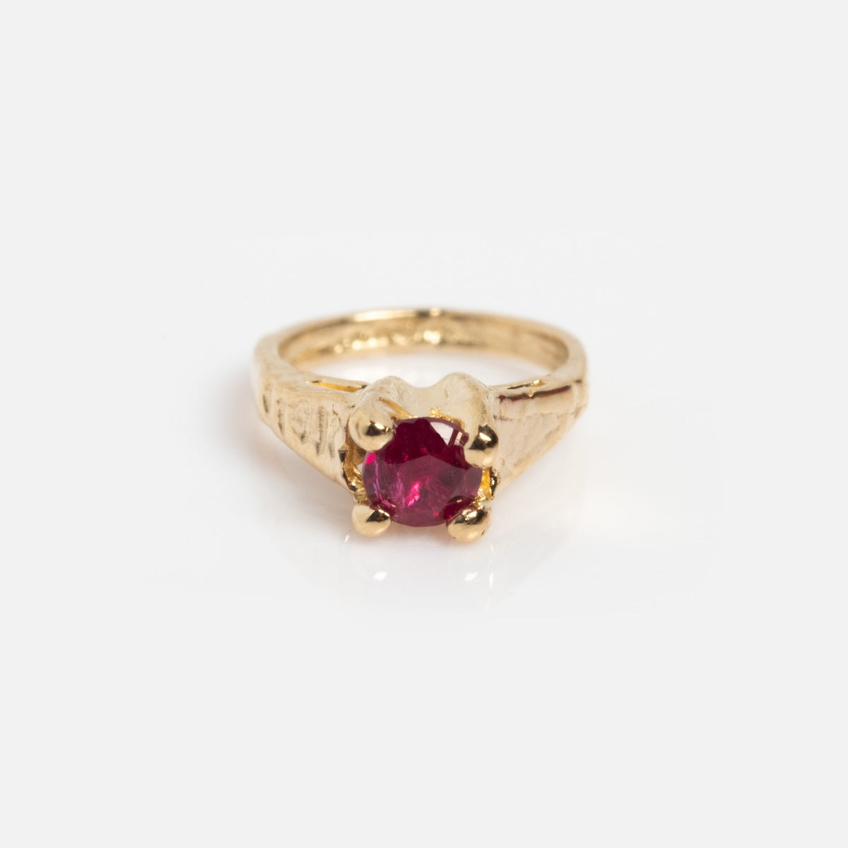 The 14k Littlest Birthstone Ring Charm by Charlie and Marcelle features a gold engraved band and a round red gemstone in a four-prong setting, gleaming against a plain white background.