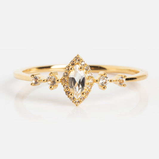The White Topaz Harlow Ring is crafted in 18k gold vermeil, showcasing a marquise-cut white topaz surrounded by accents and additional stones along the band, displayed on a white background.