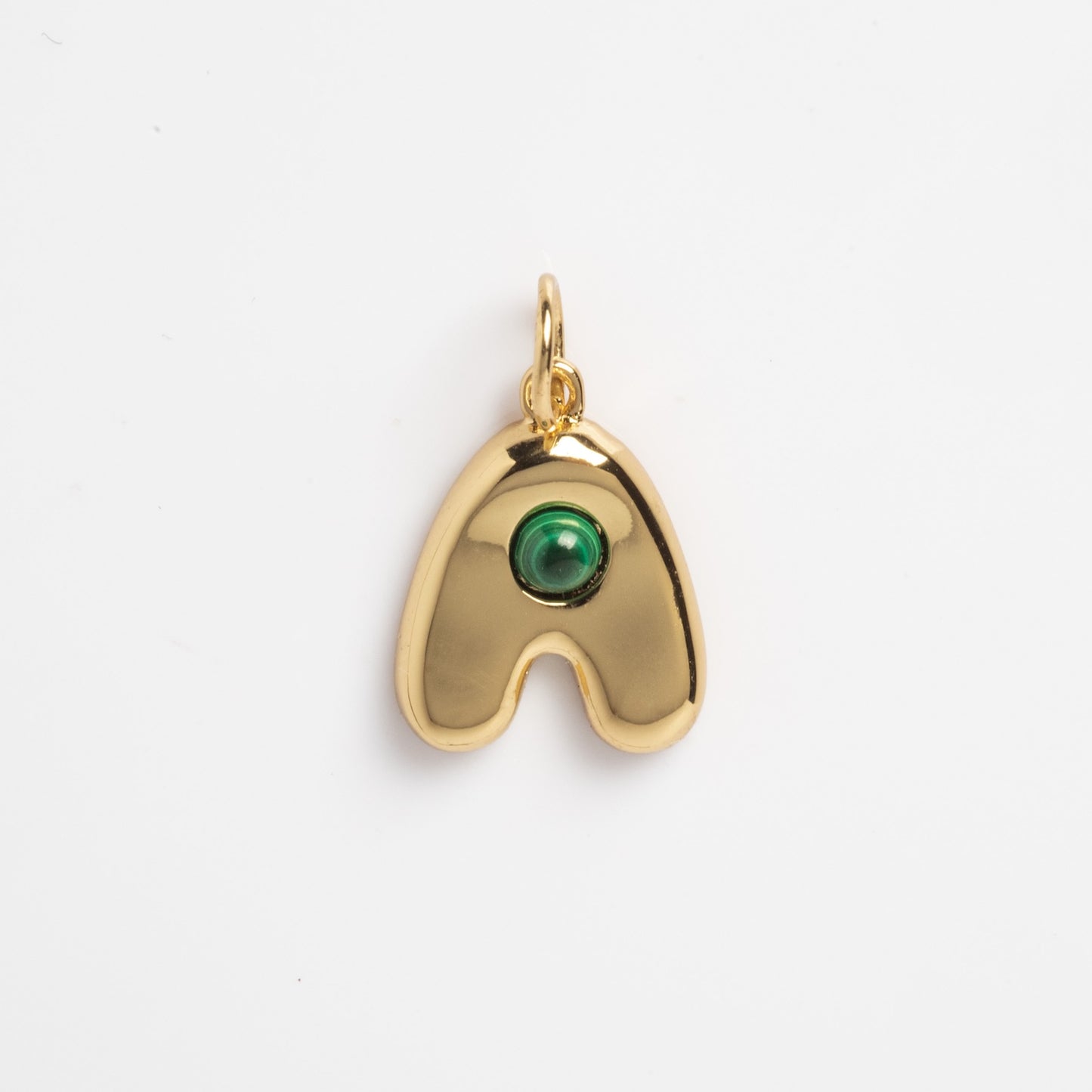 Thea Bubble Letter Charm—a gold pendant shaped like a rounded, curved "A" with a single green round gemstone set near the top center, shown against a plain white background.