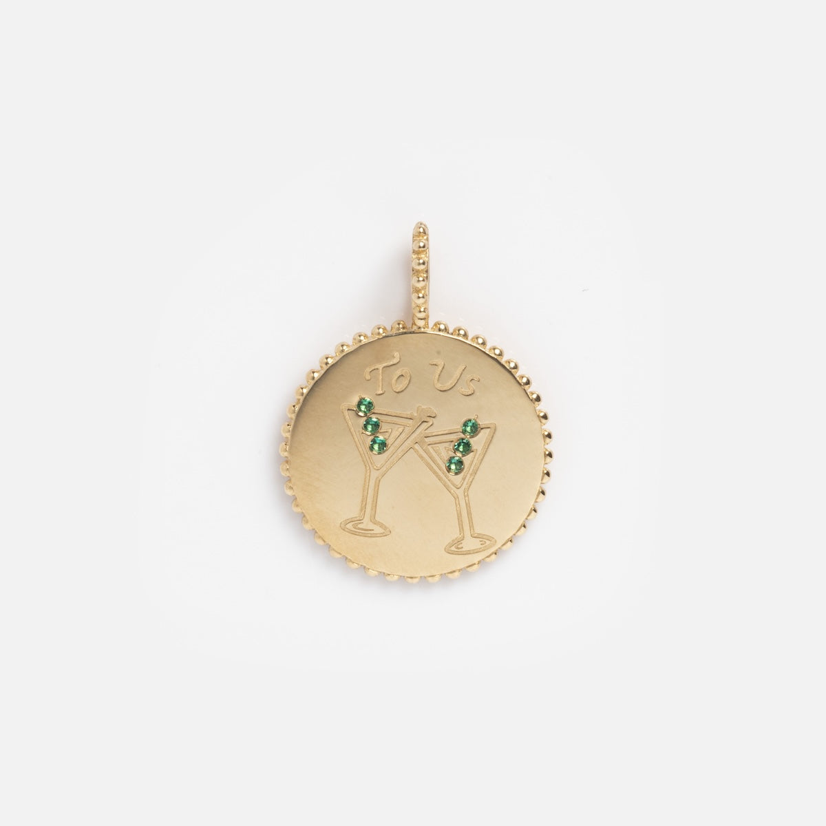 The Solid Gold Cheers To Us Coin Charm Sample is a round 9k yellow gold pendant engraved with two clinking martini glasses, 1mm lab emerald accents, and “To Us” inscribed above.