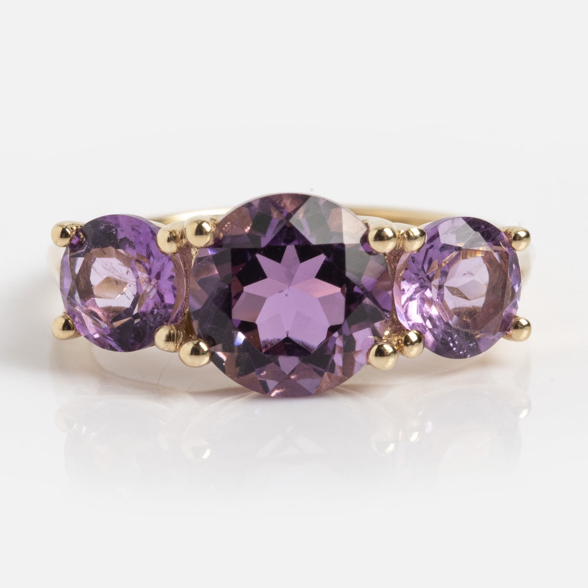 The Solid Gold Trilogy Birthstone Pinky Ring (Amethyst, Size 5) features three round purple gemstones with a larger center stone, shown against a white background.