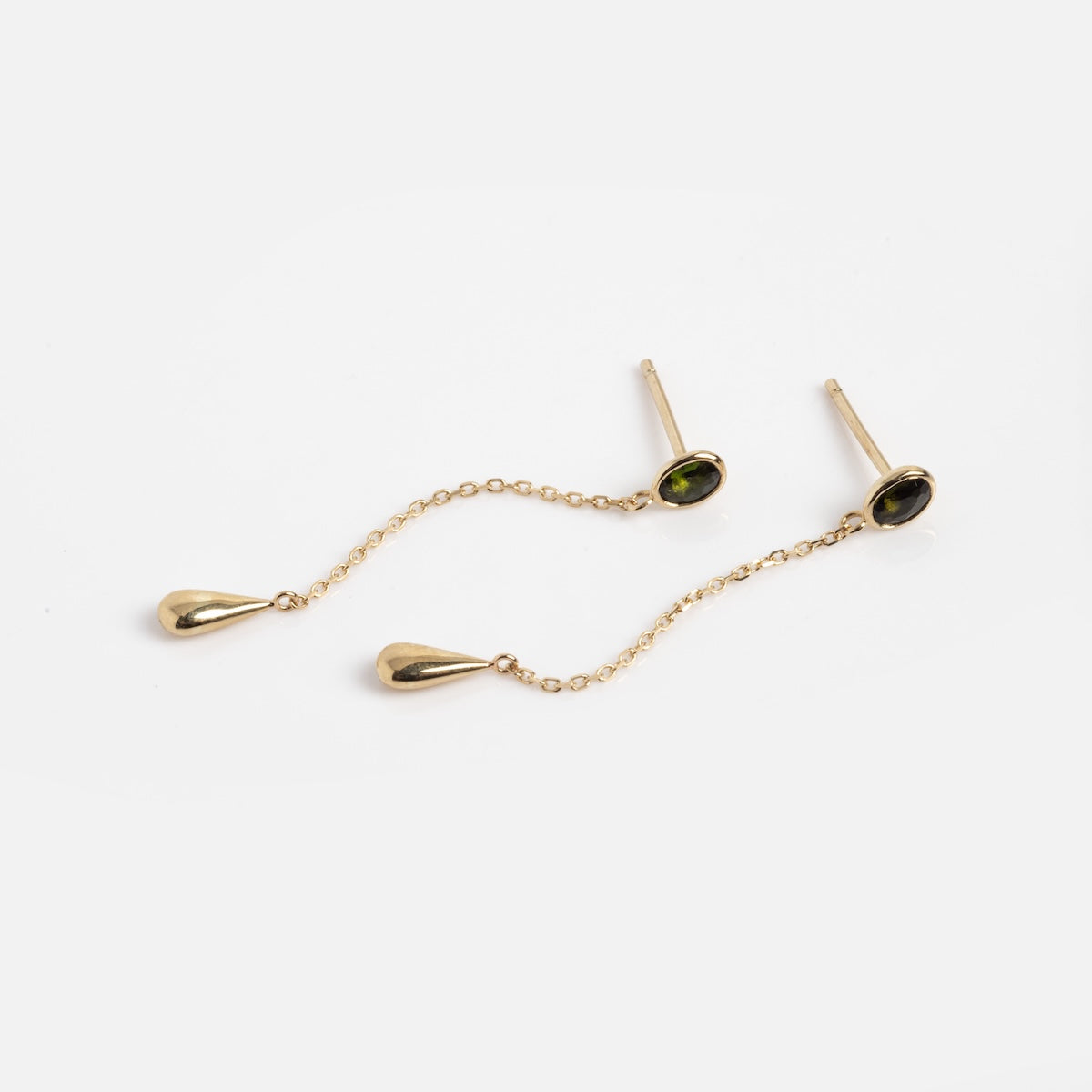 The Solid Gold Green Tourmaline Drop Earrings Sample features 9k gold drop earrings with green tourmaline oval studs and teardrop pendants linked by delicate gold chains, shown on a white background.