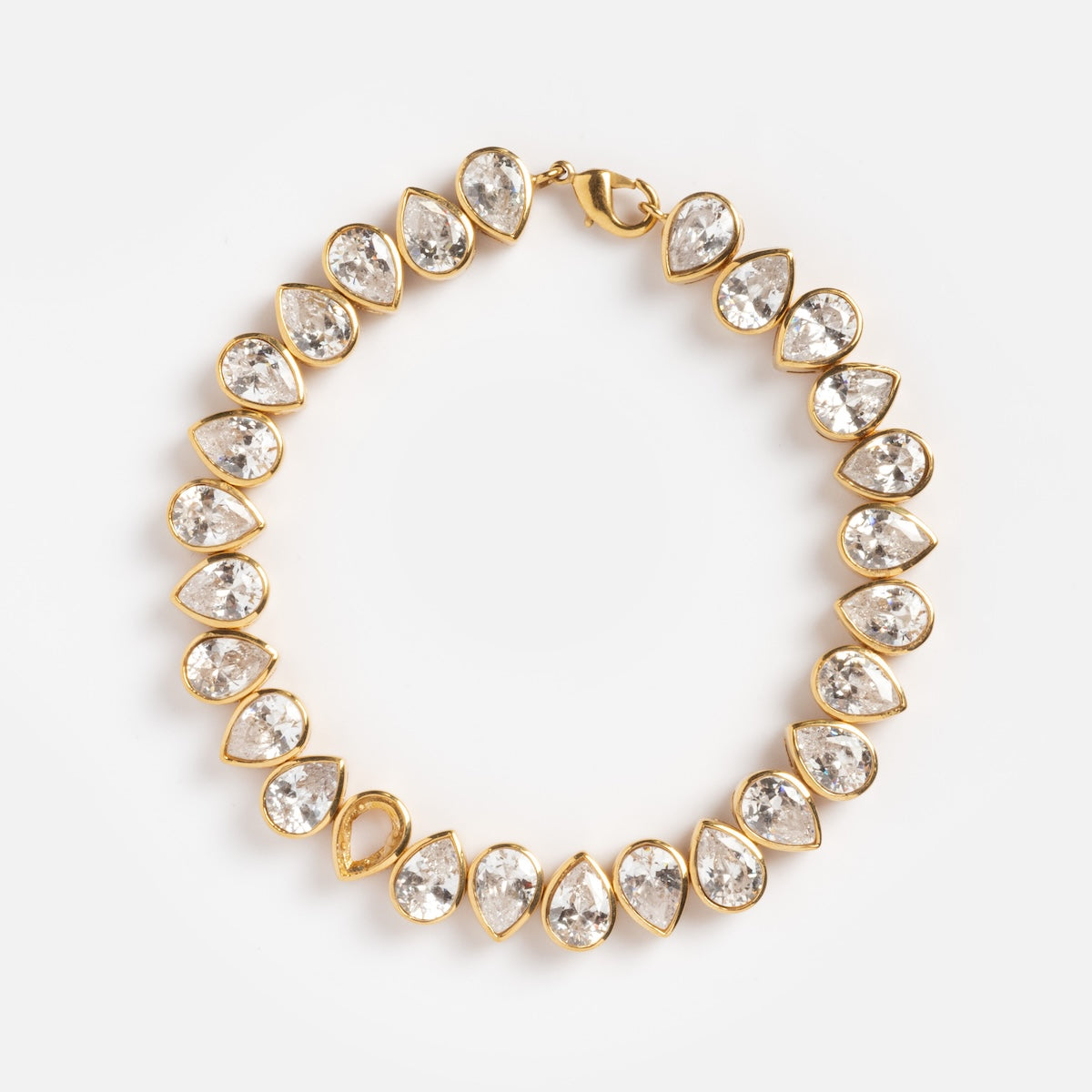 The Bezel Set Birthstone Tennis Bracelet April Sample is a yellow gold plated bracelet with alternating pear-shaped and round cubic zirconia gemstones in a symmetrical design, shown on a plain white background.