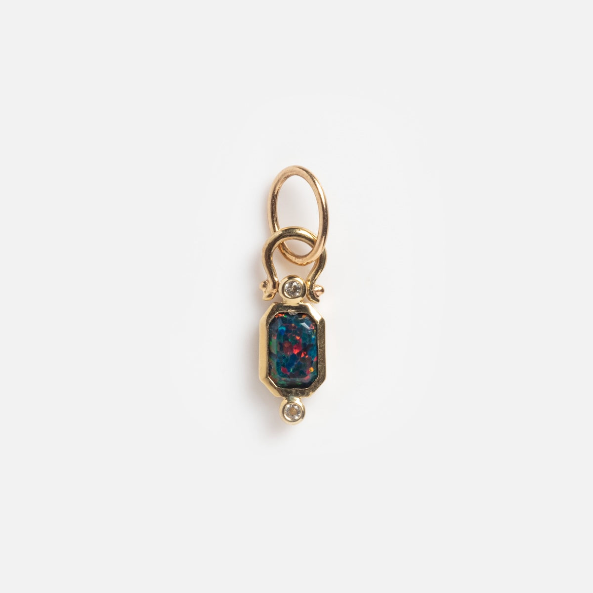 The Solid Gold Vintage Inspired Black Opal Charm Sample features a small gold pendant with an oval, multicolored black opal center, accented by two round diamonds above and below, and includes a loop for attaching to a chain.